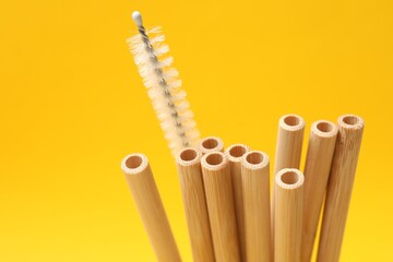 Bamboo drinking straws and cleaning brush on yellow background, closeup