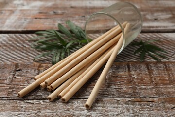Bamboo drinking straws in glass and green leaves on wooden table, closeup