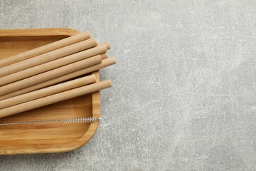 Bamboo drinking straws and cleaning brush on grey textured table, top view. Space for text