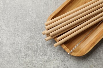 Bamboo drinking straws and cleaning brush on grey textured table, top view. Space for text