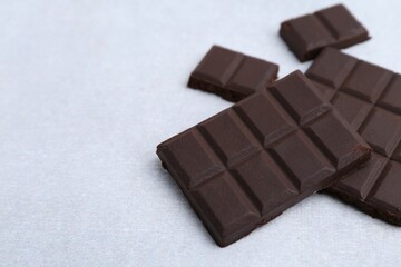 Pieces of delicious dark chocolate on light table, closeup. Space for text