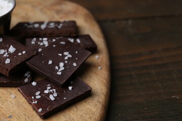Pieces of chocolate with salt on wooden table, closeup. Space for text