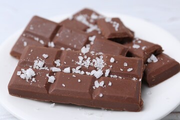 Pieces of chocolate with salt on white table, closeup