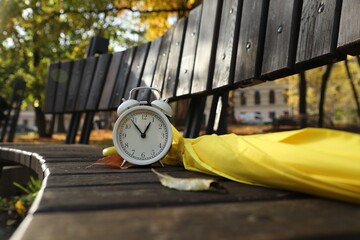 Naklejka premium Alarm clock and yellow umbrella on wooden bench outdoors