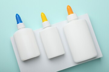Bottles of glue on light blue background, top view