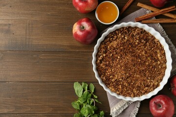 Tasty apple crisp in baking dish and ingredients on wooden table, flat lay. Space for text