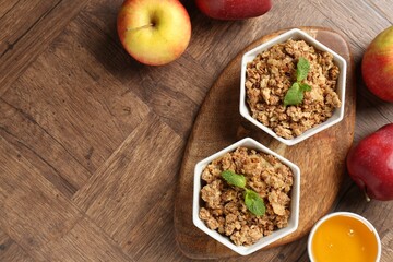 Tasty apple crisp in bowls, fresh fruits and honey on wooden table, flat lay. Space for text