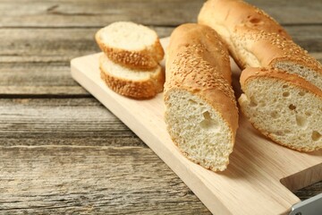 Cut fresh baguette with sesame on wooden table, closeup. Space for text