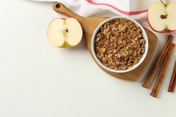 Delicious apple crisp in bowl, fresh fruits and cinnamon sticks on white table, flat lay. Space for...