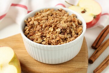 Delicious apple crisp in bowl, fresh fruits and cinnamon sticks on white table, closeup