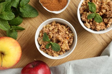 Delicious apple crisp in bowls, fresh fruits, mint and cinnamon on wooden table, flat lay