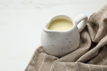 Condensed milk in jug on white marble table, closeup