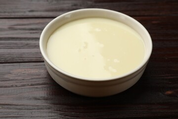 Condensed milk in bowl on wooden table, closeup