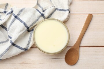 Condensed milk in bowl and spoon on light wooden table, top view