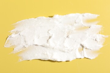 Cream on yellow background, closeup. Sample of cosmetic product