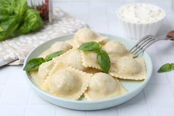 Delicious ravioli with cheese and basil served on white tiled table, closeup