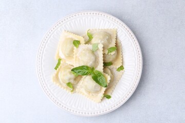Delicious ravioli with cheese and basil on light table, top view