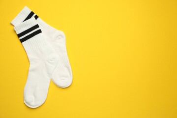 Pair of soft socks on yellow background, top view. Space for text
