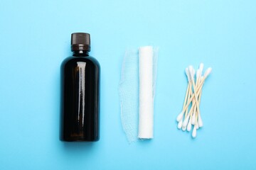 Topical iodine, bandage and cotton swabs on light blue background, flat lay