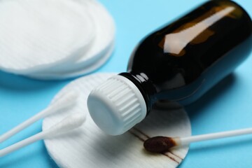 Bottle of topical iodine, cotton pads and swabs on light blue background, closeup