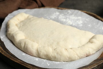 Uncooked calzone pizza on wooden board, closeup
