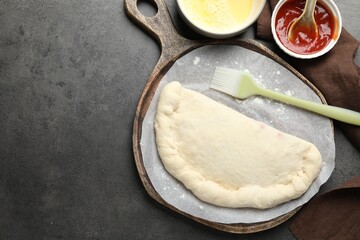 Uncooked calzone pizza, sauce and egg yolk on grey table, flat lay. Space for text
