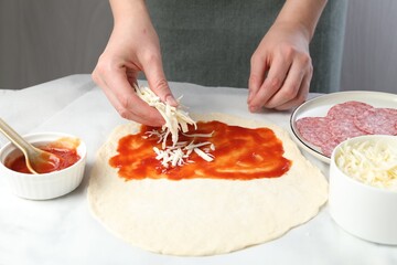 Making calzone pizza. Woman putting cheese onto dough with sauce at table, closeup