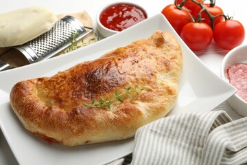 Delicious fresh calzone pizza and ingredients on white table, closeup