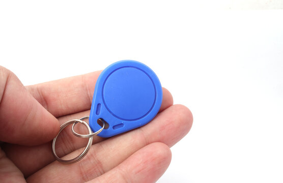 A blue RFID (Radio Frequency Identification) keychain receiver is held in a hand on a white background. Used by electronics, mechatronics, and networking engineers.