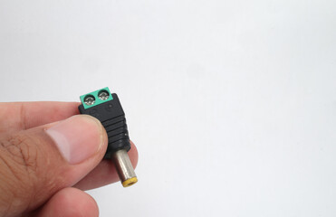 A male DC jack with green screw connection held in hand on white background.