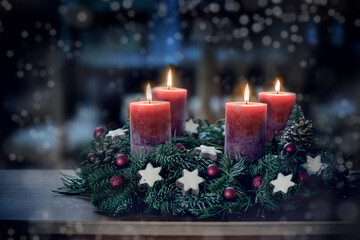 Advent wreath with the fourth lit candle and Christmas decoration outdoors in a patio at night in bluish light, snowy bokeh, copy space, colorized photo, selected focus