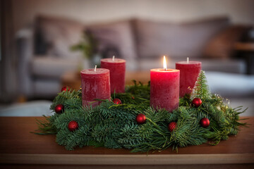 First Advent, green wreath with Christmas baubles, cinnamon star cookies and red candles, one is lit, on a table in the living room, copy space, selected focus