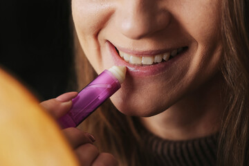 Smiling girl moisturizing lips with lip balm stick. Closeup of beautiful woman lips. Beauty and...