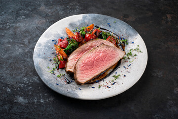 Traditional roasted veal roast served with barbecue vegetable and herbs as close-up on a design plate