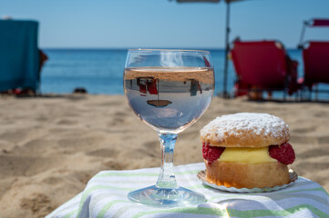 Lunch on sandy beach in Saint-Tropez with cake Tarte tropezienne filled brioche with cream and fresh red berries and glass of rose wine, summer vacation on French riviera, France
