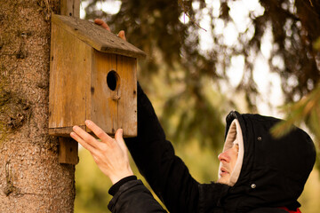 A man carefully hangs a birdhouse on a tree, ensuring a safe and inviting home for birds, surrounded by lush greenery and natural serenity.


