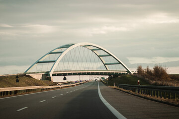 Obraz premium A highway bridge stretches across the road, seamlessly integrating into the landscape. The structure blends with the scenery, providing an essential passage for vehicles on their journey.