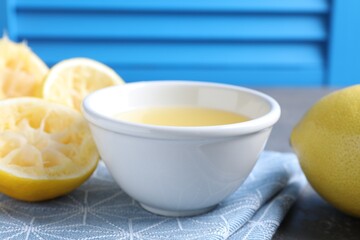 Fresh lemon juice in bowl and fruits on table, closeup