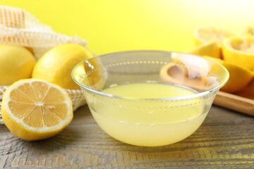 Bowl with fresh lemon juice and fruits on wooden table, closeup