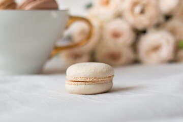 Sweet dessert, vanilla macaroons, mug and white roses on bed background. Romantic morning breakfast at bed.