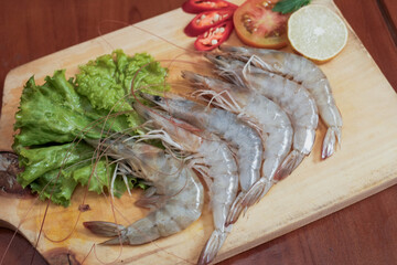 Fresh raw shrimp on wooden cutting board with lettuce, slice of red chili, tomato slice and slice lemon on the side, preparing of fresh seafood cook.