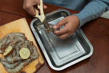 Process of hands women peel shrimps shell with scissors on the wooden table. Woman cleaning shrimp for seafood cooking