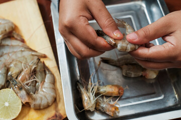Process of hands women peel raw shrimp shell on the wooden table. Woman cleaning shrimp for seafood cooking