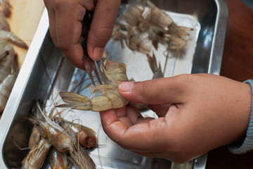 Process of hands women peel shrimps shell with fork on the wooden table. Woman cleaning shrimp for seafood cooking