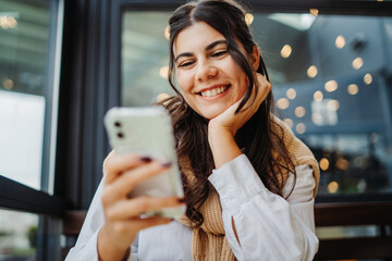 Young caucasian woman using phone in cafe to talk or send messages sms