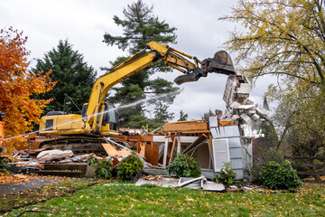 Large yellow excavator working on the last section of a house demolition tearing chimney down,...