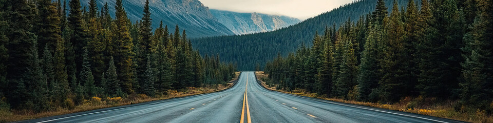 Fototapeta premium Empty highway leading into the distance, framed by towering pine trees and a stunning mountain range.