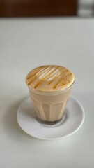 Hot caramel macchiato in a clear glass on a white saucer served in a cafe