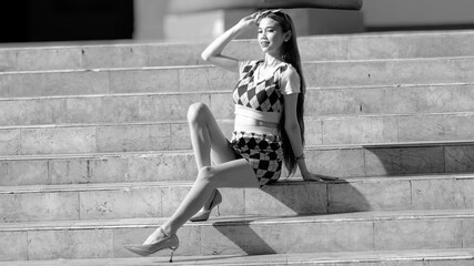 In black and white portrait of a young woman with long hair setting on a staircase of a building