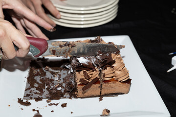 Un delicioso pastel de chocolate es cuidadosamente cortado, simbolizando el comienzo de un momento compartido y especial. La textura rica del chocolate y la disposición elegante resaltan el placer de 